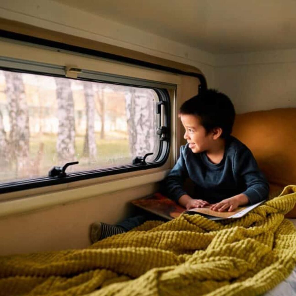Little boy looking out the window of a RV while holding a book